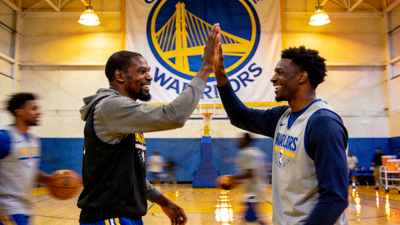 篮球巨星凯文·杜兰特在训练馆与新队友击掌，背景是球队巨大的队徽